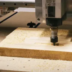 Precyzyjny frez CNC pracuje nad drewnianym elementem, tworząc rowki i kształty. Wióry drewna unoszą się wokół.
