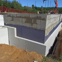Izolacja fundamentów w starym domu w trakcie prac. Ściany z bloczków betonowych, izolacja przeciwwilgociowa i termiczna.