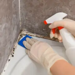 Rękawiczki i gąbka do czyszczenia fug z pleśni w łazience. Spray z płynem czyszczącym w dłoni.