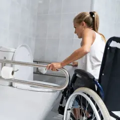 Kobieta w wózku inwalidzkim korzysta z uchwytów przy toalecie w łazience.