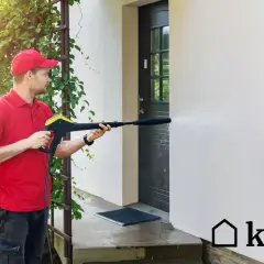 Mężczyzna w czerwonej koszulce i czapce myje elewację domu myjką ciśnieniową. Sprawdź, jaka jest mycie elewacji cena.