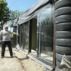 Budowa **earthship** z opon. Mężczyzna wskazuje na szklaną ścianę domu z opon.