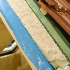 Warstwa izolacyjna z materiału pu w przekroju dachu, widoczna pianka, folia niebieska i dachówka.