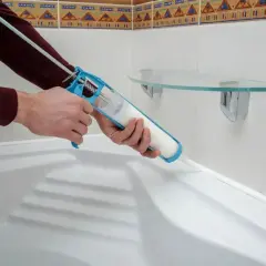 Dłoń z pistoletem do silikonu uszczelnia wannę. Czas, ile schnie silikon, zależy od warunków.