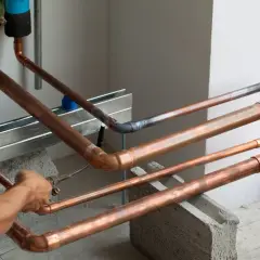 Instalator lutuje miedziane rury. W tle widać niebieskie filtry.