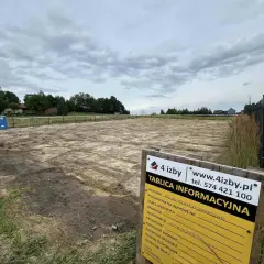 Tablica informacyjna budowy placu budowy z koparką w tle.
