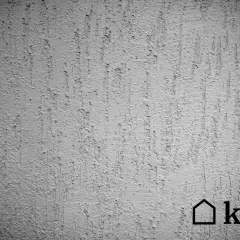 Szara ściana z fakturą tynku kornik, imitującą ślady po żerowaniu owadów. Widoczne pionowe, nieregularne zagłębienia.