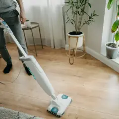 Osoba myje panele podłogowe mopem parowym. Czy mopem parowym można myć panele? Tak, ten sprzęt skutecznie czyści drewniane powierzchnie.