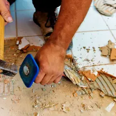 Skuwanie płytek cena: pracownik używa młota i dłuta do usuwania starych płytek z podłogi.