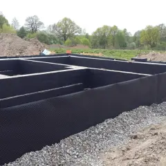 Fundament z czarną izolacją i folią kubełkową. W tle hałdy ziemi i drzewa. To solidna baza, jak izoplast b.