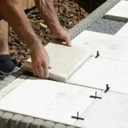 Mężczyzna układa płyty tarasowe na podsypce, tworząc równą nawierzchnię.