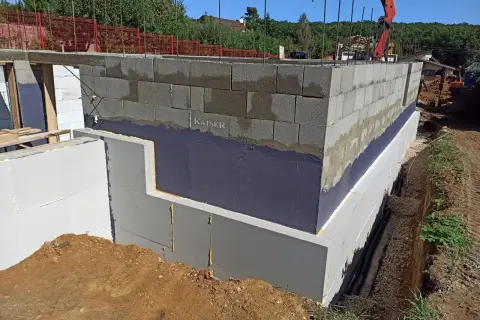 Izolacja fundamentów w starym domu w trakcie prac. Ściany z bloczków betonowych, izolacja przeciwwilgociowa i termiczna.