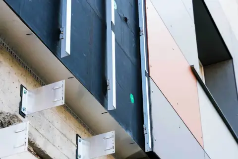 System mocowania elewacji wentylowanej. Metalowe wsporniki przytwierdzone do betonowej ściany, tworzące przestrzeń wentylacyjną pod panelami elewacyjnymi.