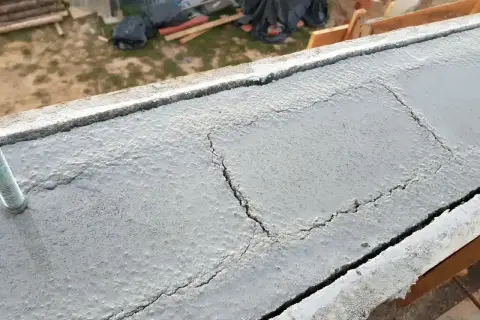 Pęknięcia na świeżym betonie wieńca budowlanego, widoczny pręt kotwiący.