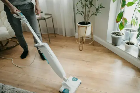 Osoba myje panele podłogowe mopem parowym. Czy mopem parowym można myć panele? Tak, ten sprzęt skutecznie czyści drewniane powierzchnie.