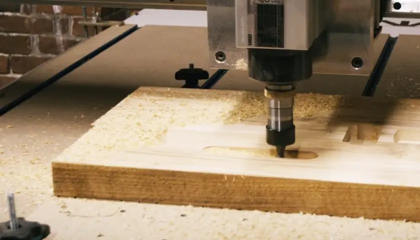 Precyzyjny frez CNC pracuje nad drewnianym elementem, tworząc rowki i kształty. Wióry drewna unoszą się wokół.