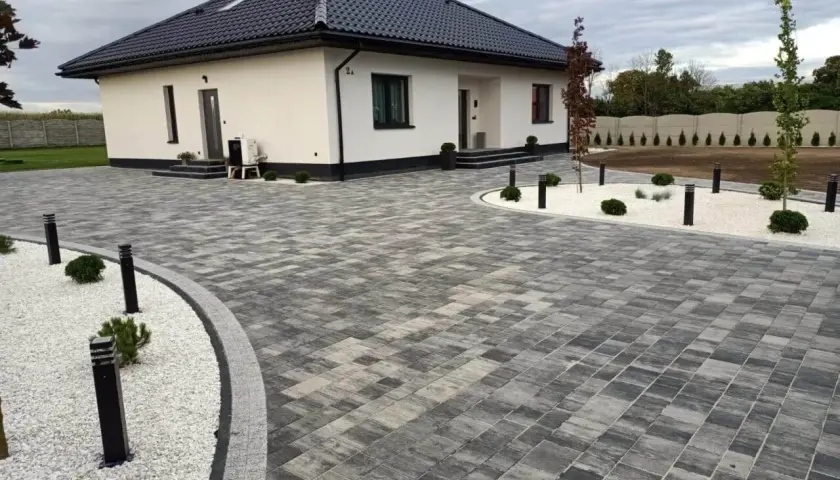 Nowoczesny dom z podjazdem z behatonu, oświetlonym stylowymi lampami.