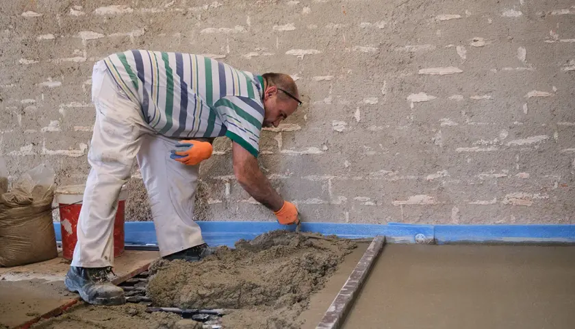 Budowlaniec pokazuje, jak wyrównać podłogę pod panele bez wylewki, używając zaprawy i łaty.