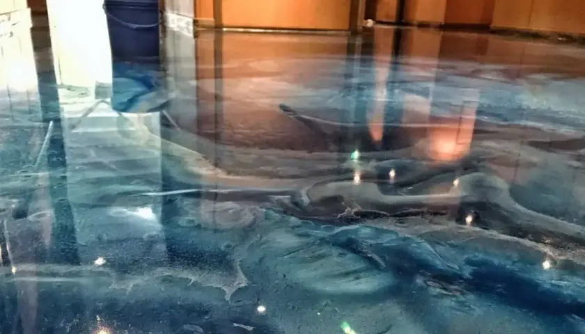 Błękitna żywica w garażu tworzy efekt fal oceanu. Widać niebieskie wiadro i odbicia światła.