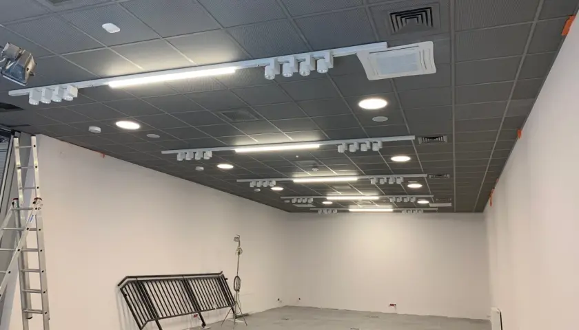Sufit Armstrong z oświetleniem szynowym i klimatyzacją w trakcie montażu. Widać drabinę i balustradę.