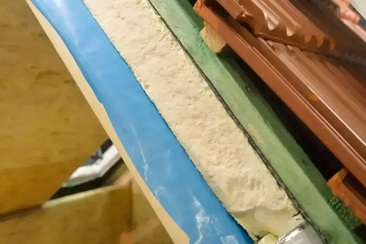 Warstwa izolacyjna z materiału pu w przekroju dachu, widoczna pianka, folia niebieska i dachówka.