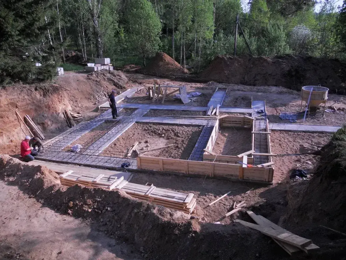 Budowa fundamentów domu. Widać zbrojenie i szalunki. Pracownicy nadzorują chudziak.