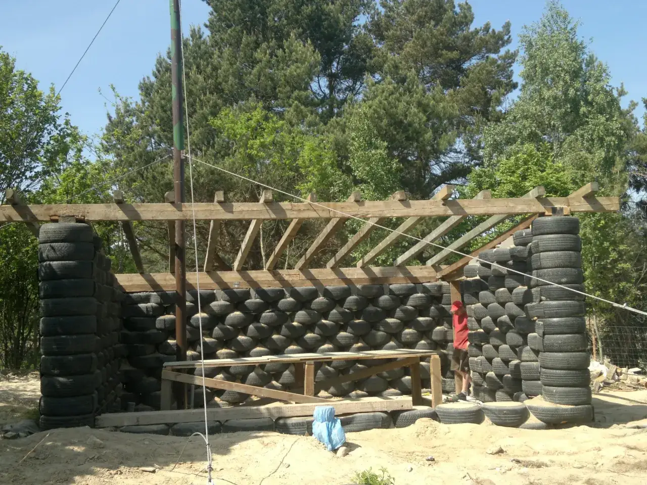 Budowa ekologicznego domu typu earthship z opon. Widać ściany z opon, drewnianą konstrukcję dachu i młodego budowniczego.