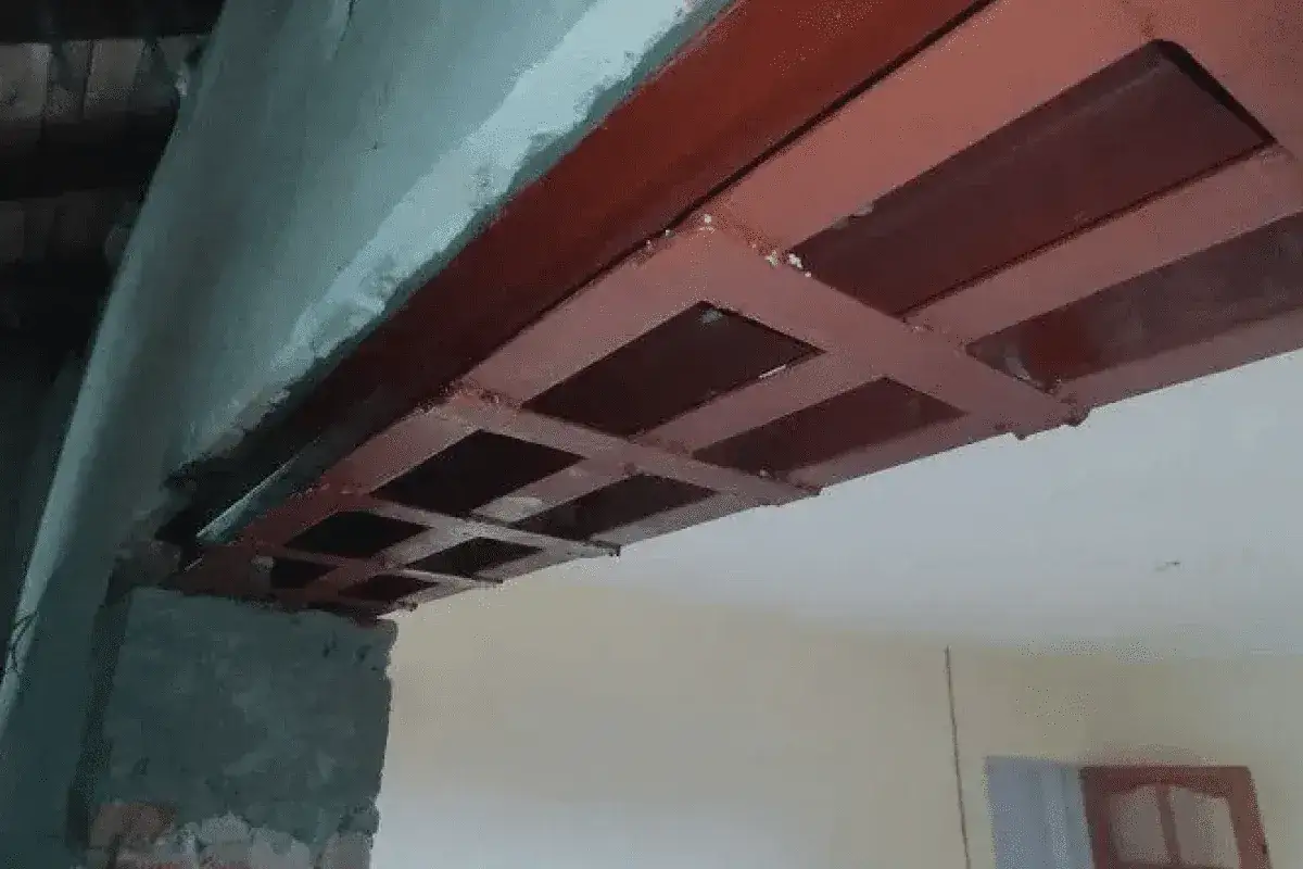 Metalowa konstrukcja podciągu wzmacnia strop. Widać ceglaną ścianę i fragment sufitu.