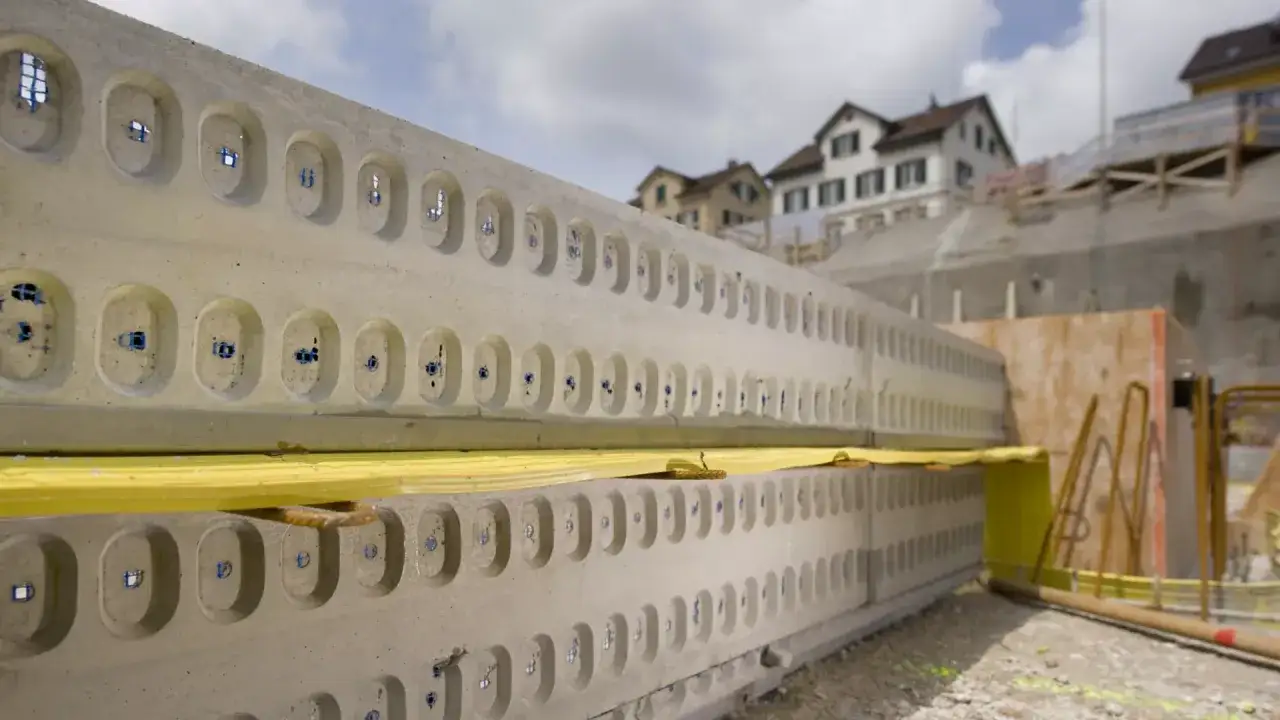 Betonowe elementy z otworami, przygotowane do budowy. W tle domy i plac budowy.